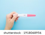 Young adult woman hand holding pregnancy test with one stripe on light blue table background. Pastel color. Negative result. Closeup.