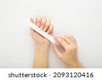 Small photo of Young adult woman hand using nail file and filing nails on white towel background. Closeup. Point of view shot. Care about fingernails.