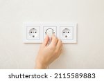 Young adult woman hand holding and plugging white electrical plug in wall outlet socket at home. Closeup.