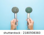 Young adult woman hands holding new and old shower heads on light blue table background. Pastel color. Compare two objects with and without limescale. Dirty and clean. Closeup. Point of view shot.