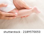 Small photo of Young adult mother finger applying white medical ointment on newborn bare leg. Red rash on skin. Allergy from milk formula or mother milk. Care about baby body. Closeup. Top view.