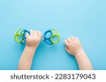 Baby boy hands playing with colorful rattle dumbbell on light blue table background. Pastel color. Closeup. Point of view shot. Toy of development for infant.