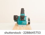 Small photo of Electric jointer on old wooden plank on white table at light gray wall background. Closeup. Preparing material for repair work of home. Front view.