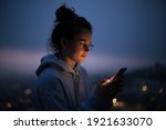 Small photo of Beautiful young woman use smartphone at night. Millennial generation z female scroll through news feed on app on her phone. Cinematic film look photo of pretty woman at sunset use phone