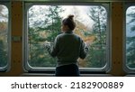 Small photo of Cinematic and symmetrical beautiful shot of female traveler, travel blogger and inspired adventurer hang out of train window, look at amazing landscape of autumn mountains