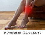 Small photo of Woman siting on couch and holding shin with her hand closeup. Prevention of varicose veins concept.