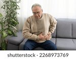 Small photo of Elderly men have abdominal pain sitting on the sofa in the house. Concept Problems of the digestive tract in older people, health care.