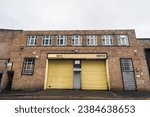 Small photo of Birmingham, England, November 4th 2023. Front view of a Hertz car rental facility with distinctive yellow garage doors, situated in a brick building.