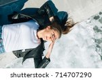 Small photo of The lovely girl in a white t-shirt and a black leather jacket has lain down on a pier by the concerning sea. She covers eyes from bright beams of the sun and gently smiles.