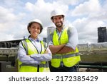 Small photo of Portrait diversity male and female engineer work together on roof top of site line . Portrait of engineer with green safety vest and white hard hat at building site looking at camera