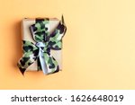 Small photo of Gift box with khaki ribbon on the yellow background. Defender of the Fatherland Day, February 23. Space for text.