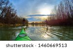 Small photo of Man and boy rowing with a paddle on the stand up paddle board (paddleboard, SUP) in the Danube river at calm cold winter evening. View from bow of green kayak