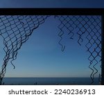 View of the summer beach through a torn metal mesh net fence. black sea coast from behind metal wire fence.