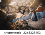 Small photo of Cordless Chainsaw. Close-up of woodcutter sawing chain saw in motion, sawdust fly to sides. Chainsaw in motion. Hard wood working in forest. Sawdust fly around. Firewood processing.