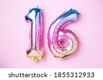 Creative layout. Rainbow foil balloon number, digit sixteen. Birthday greeting card with inscription 16. Anniversary concept. Top view. Stylish colored numeral on pink background. Numerical digit.
