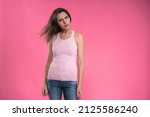 Small photo of Aggrieved, troubled, young woman in pink sleeveless T-shirt looking at camera with heavy head bowed sideways, and hands down isolated on pink background. Karen syndrome woman.