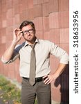 Small photo of Hipster businessman with look of verjuice posing outdoors. Man in white shirt touching his glasses and keeping one hand on hip.