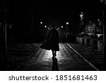 dark silhouette of a male detective in a coat and hat in the rain on a night street in the style of Noir