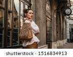 Outdoor fashion portrait of elegant, luxury woman wearing trendy white shirt, holding stylish beige, brown reptile, snakeskin, python print bag, handbag, posing in street. Copy, empty space for text 