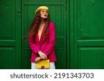 Fashionable confident woman wearing trendy outfit with yellow sunglasses, beret, shoulder bag, pink fuchsia color blazer, posing near green door. Copy, empty space for text