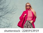 Small photo of Fashionable confident blonde woman wearing trendy pink sunglasses, fuchsia color coat, turtleneck, zebra print trousers, holding faux leather tote, shopper bag. Copy, empty space for text