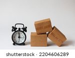 Small photo of cardboard boxes and black alarm clock on white background, fast shipping. transportation speed. storage time in the warehouse. delayed delivery. quick carriage.