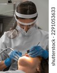 Small photo of Female dentist and assistant removing dental calculus from teeth. Visit is in proffessional dental clinic. Woman sits on dental chair. Drilling and treatment of tooth, filling. Vertical photo
