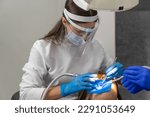 Small photo of Female dentist and assistant removing dental calculus from teeth. Visit is in proffessional dental clinic. Woman sits on dental chair. Drilling and treatment of tooth, filling.