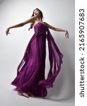 Small photo of Full length portrait of beautiful girl wearing flowing fantasy purple ball gown. Standing with gestural hand poses, fro ma low angle perspective Isolated on studio background.