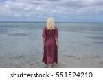 portrait of a blonde girl wearing a long purple dress standing in he ocean and touching the water