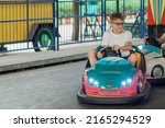 Portrait of teenage boy in glasses driving an electric car in amusement park. Child on Bumper car