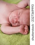 Small photo of Close-up portrait of a cranky 1-month old baby boy lying on green towel. Infant with newborn acne on his face in bed. Skin problems of newborns. Fussy little kid shortly after birth. Emotions concept.