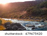 Small photo of Riverside view of the Rio Grande River in New Mexico. The sun dips is just about to dip below the gorge rim as the river babbles across rocks in the forefront.