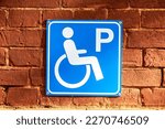 Disabled parking icon on the red brick wall close up. Wheelchair symbol