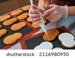 applying a layer of glaze to a confectionery product using a pastry bag. A row of gingerbread cookies on the kitchen table. Confectioner's inventory. Product surface decoration