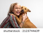 A cute young woman kisses and hugs her mongrel dog. Love between owner and dog. Isolated on white background. Studio portrait. Girl huging new lovely member of family. Pet care and animals concept