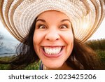 Portrait of a woman in a hat close-up, full-face, on a wide-angle lens. Distorted proportions, funny face. A charming smile with perfect teeth.