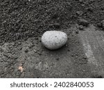 Small photo of Grey ellipse stone isolated on black sands background