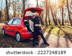 Happy loving couple relaxing in car trunk hugging in autumn forest. Man and woman travel by auto. Young people enjoy fall trip