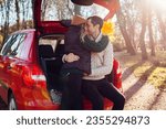 Happy loving couple enjoying date in car trunk hugging in autumn forest at sunset. Husband and wife travel by auto.