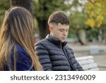 Small photo of Boy with a melancholic gesture sitting on a bench in the square next to a girl.