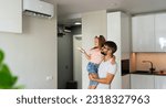 Small photo of Father kept to hand little girl and turn on air conditioner using remote control. Happy family adjust comfortable temperature of cooler system