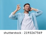 Happy attractive tanned handsome man in casual basic t-shirt headphones listen cool sound show gesture Okay posing isolated on blue studio background. Copy space Banner Mockup. Music concept