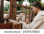 A woman in a sweater petting a goat behind a fence in a barnyard