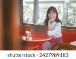 Freelance concept, A delighted young woman smiles at the camera, enjoying her time working on a laptop in a sunlit café corner.