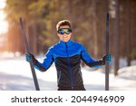 Portrait happy male athlete with cross country skis in hands and goggles, training in snowy forest. Healthy winter lifestyle concept.