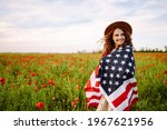 Young woman in hat with the American flag in in the poppy field. Fourth of July. Freedom. Beautiful sunset. Independence Day. Patriotic holiday.