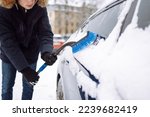 Portrait of young man cleaning snow off  car during winter snowfall. Transport, winter, weather, people and vehicle concept.