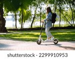 Young female legs on an electric scooter. Beautiful woman rides an electric scooter in the park on a sunny day. Ecological transport. Active lifestyle.