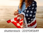 Young woman with American flag  and sparklers on the beach. Patriotic holiday. USA celebrate 4th of July. Independence Day concept